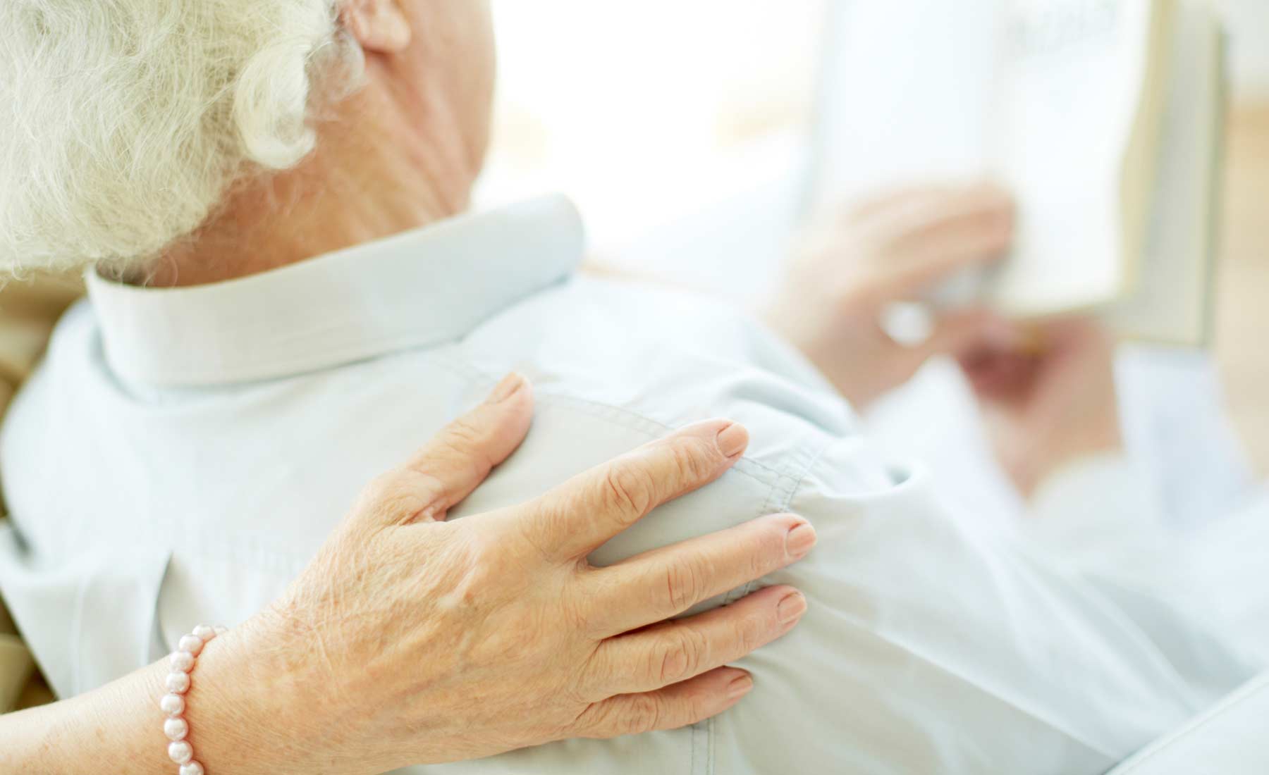 An elderly lady places her hand on her husband's shoulder.